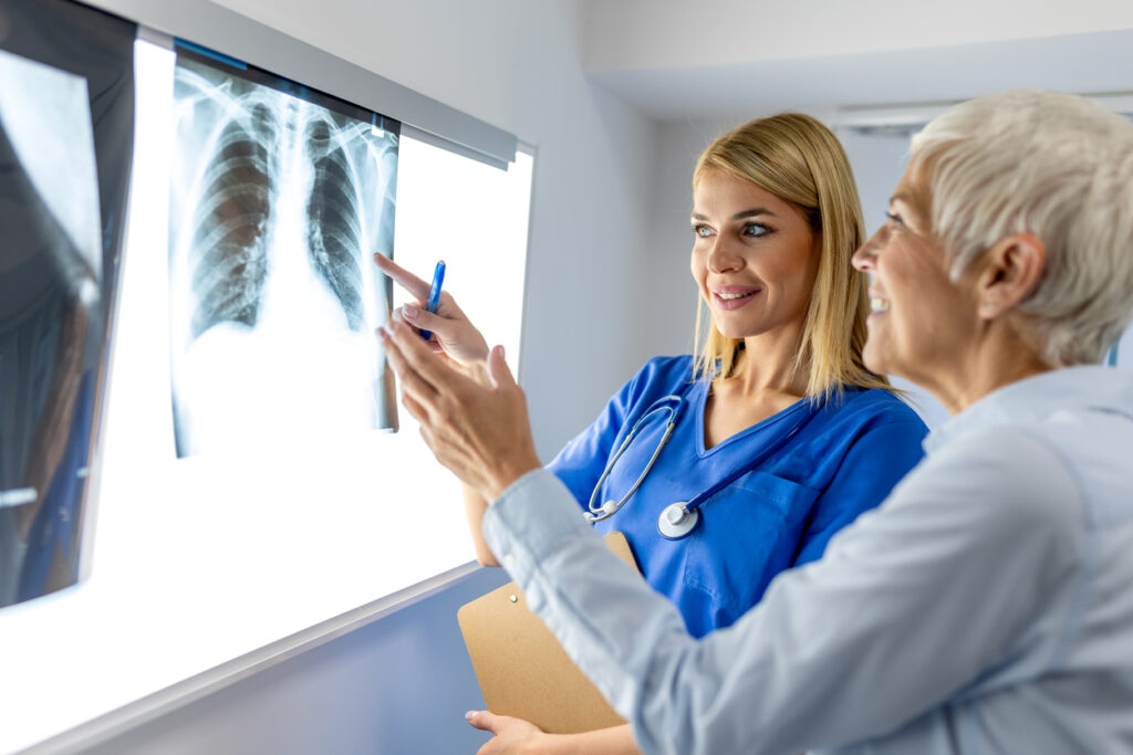 Doctor woman checking x-ray film in medical laboratory at hospital, explaining the results of scan lung on screen to senior patient. Urgent Care with X-Ray Near Me